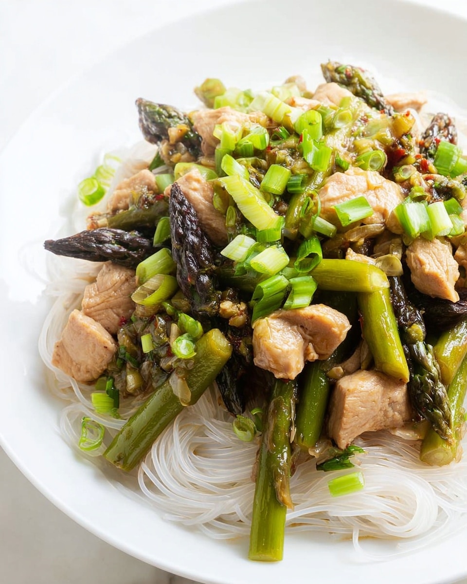 On a white plate with a white marbled texture under it, there is one layer of thin white noodles that form the base at the bottom right side. On top of the noodles is a layer of cooked asparagus stalks with darkened tips, showing charred texture and deep green color. Mixed with the asparagus are chunks of light brown cooked meat, with a slightly moist and tender look. The dish is topped with chopped bright green spring onions scattered evenly over the meat and asparagus, adding a fresh and crisp contrast to the colors and textures. photo taken with an iphone --ar 4:5 --v 7