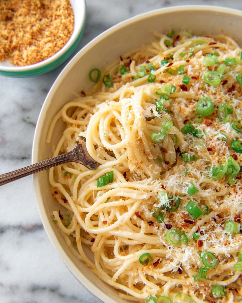 A large white pan filled with spaghetti pasta mixed with a light sauce is shown. The top layer is covered with finely grated white cheese and green chopped scallions scattered all over. There are small brown toasted crumbs sprinkled unevenly across the dish. The pan is placed on a white marbled surface next to small white bowls that hold more crumbs. Photo taken with an iphone --ar 4:5 --v 7