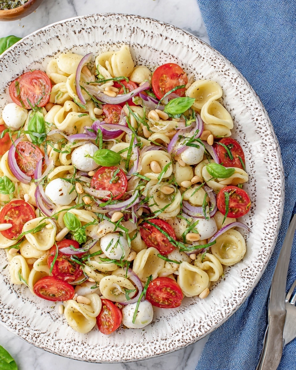 A close-up of a white spoon holding a small serving of pasta salad with three main layers: the bottom layer is made of shell pasta in light yellow with a smooth texture; the middle layer is made of halved red cherry tomatoes and small white mozzarella balls; the top layer consists of thin, green basil strips scattered across, along with a few pine nuts. The pasta salad is lightly sprinkled with black pepper, and the background shows a blurred fresh basil plant against a white marbled surface. photo taken with an iphone --ar 4:5 --v 7