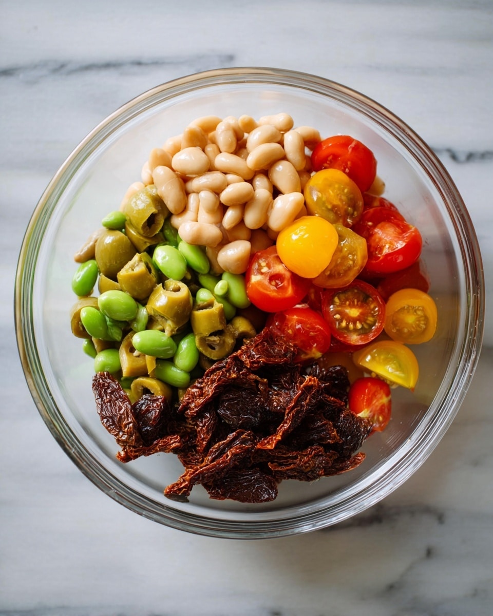 A clear glass bowl on a white marbled surface holds four distinct sections of ingredients. One section is bright green cut olives with a slightly rough texture, placed next to a section of smooth beige beans. Adjacent to the beans are halved cherry tomatoes in red and yellow, showing their juicy, shiny interiors. Next to the tomatoes is a dark brown pile of sun-dried tomatoes with a wrinkled, dry texture. The bowl is viewed from above, showing each ingredient clearly separated, bright, and fresh photo taken with an iphone --ar 4:5 --v 7