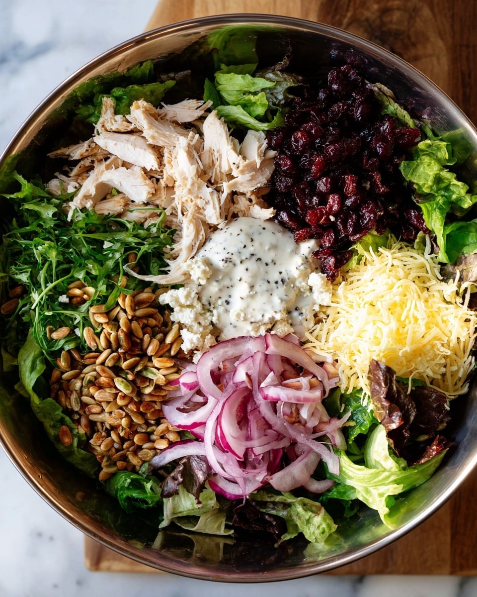 A large round silver bowl sits on a white marbled surface, filled with layers of fresh green and purple lettuce leaves forming a base. On top, shredded white chicken meat is placed on one side, opposite a pile of dark red dried cranberries. Next to the chicken is a mound of crunchy golden sunflower seeds, and on the other side is a heap of pale yellow shredded cheese. Bright purple thinly sliced red onions fan out beside the seeds, and a creamy white dressing with black pepper specks is spread in the center, blending slightly with the other ingredients. photo taken with an iphone --ar 4:5 --v 7