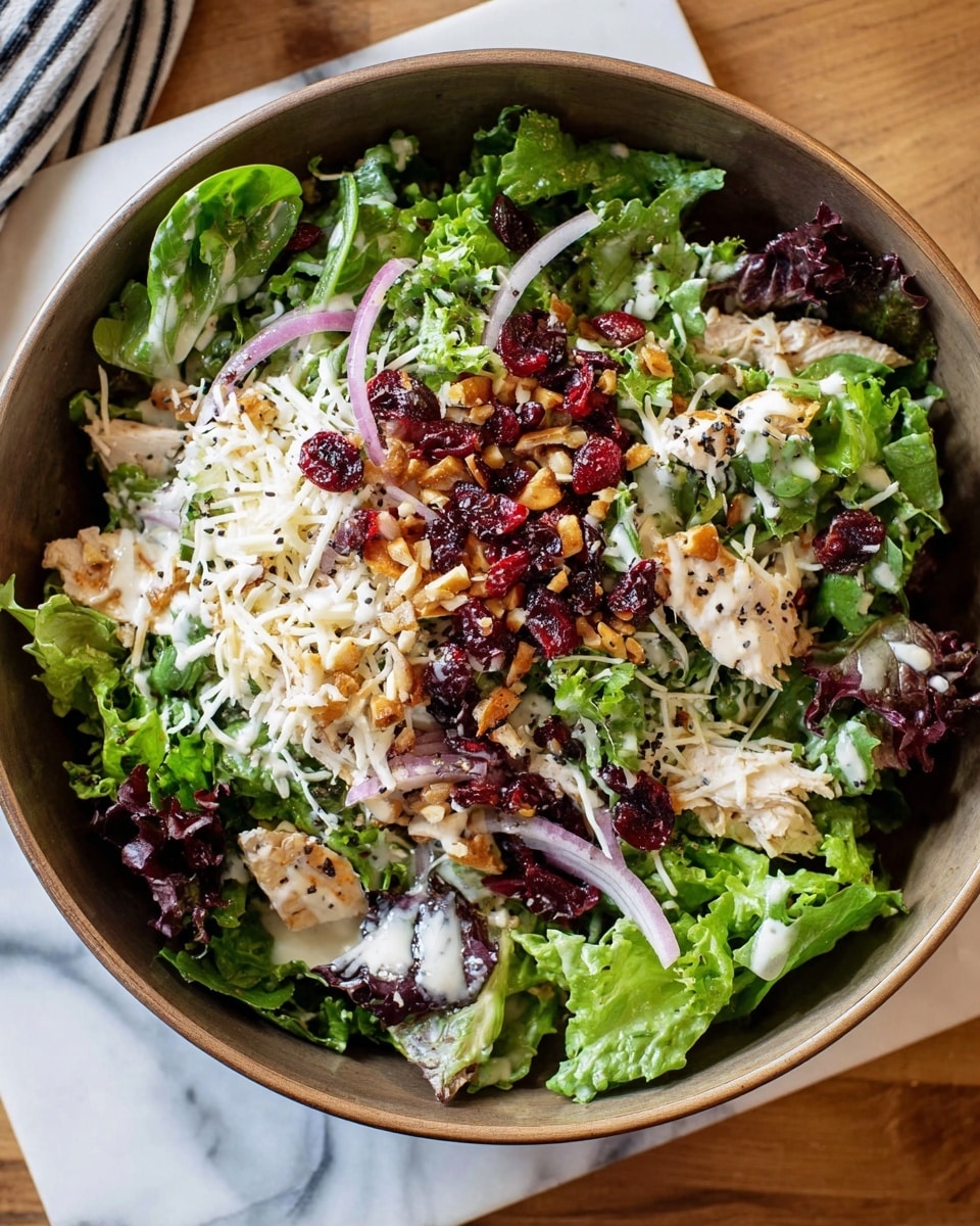 A large bowl filled with three main layers: the bottom layer has mixed green and purple leafy lettuce with soft textures; the middle layer consists of scattered thin red onion slices and small, light-colored pieces of chicken; the top layer shows white shredded cheese, dried red cranberries, and small golden pine nuts all mixed with creamy white dressing dotted with black pepper. The bowl is on a wooden surface with a white marbled texture visible around it. Photo taken with an iphone --ar 4:5 --v 7