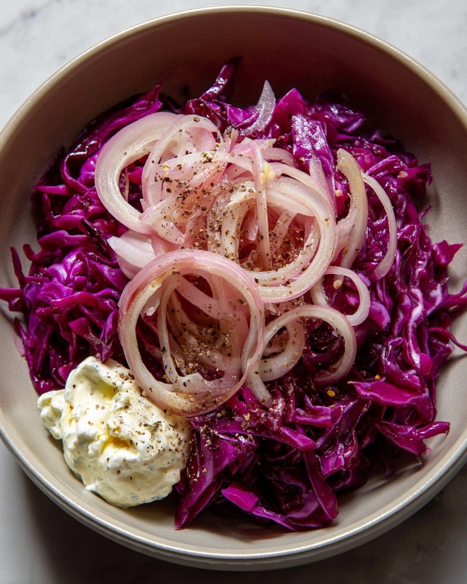 A white bowl holds two layers of thinly sliced vegetables: the bottom layer is bright purple shredded cabbage with a crisp texture, topped by thin, pale pink rings of red onion scattered loosely. On the side of the onions, there is a small dollop of white creamy dressing with a slightly chunky texture. Some light seasoning with small specks of black pepper is sprinkled over the onions and dressing. The bowl is placed on a white marbled surface. photo taken with an iphone --ar 4:5 --v 7