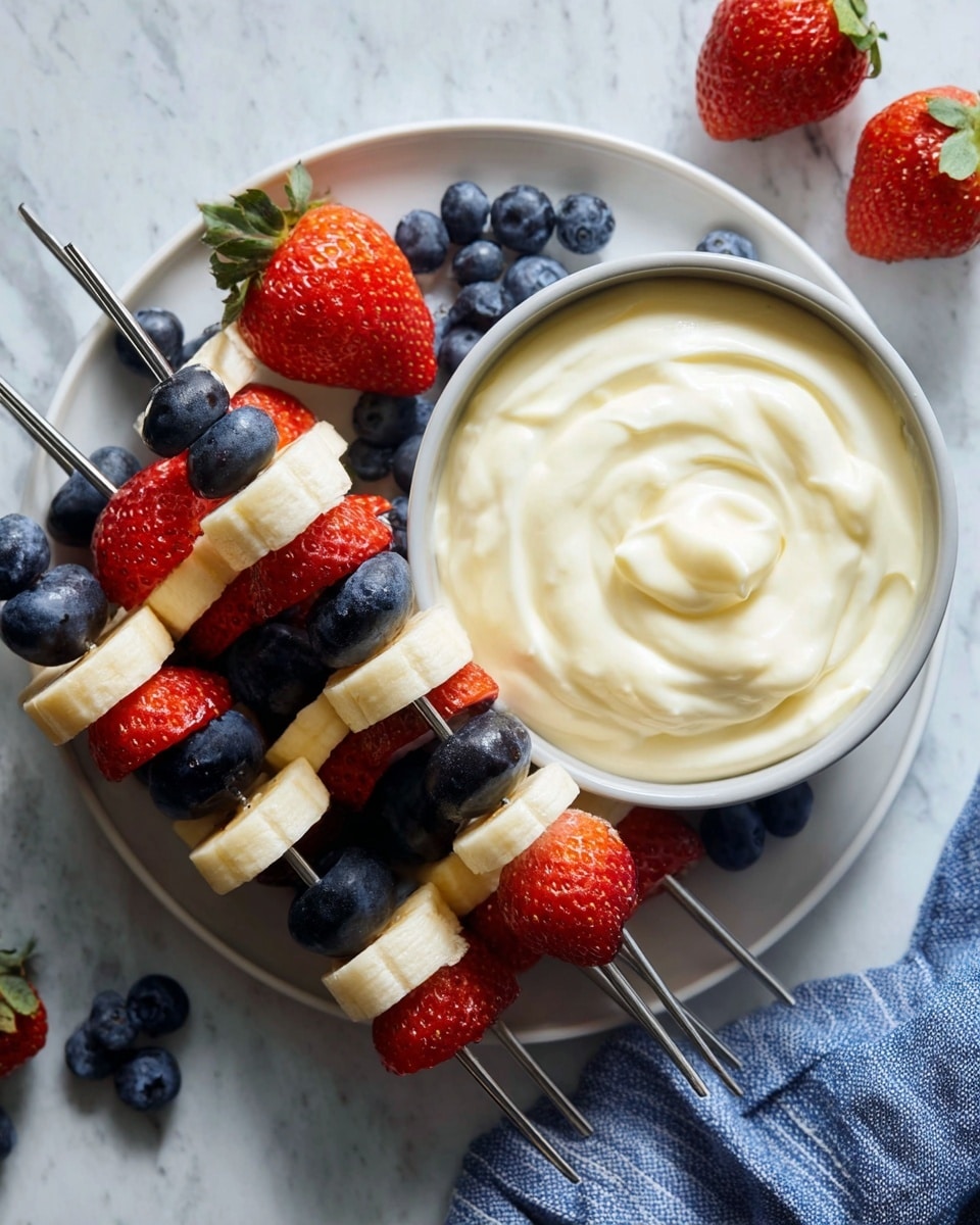 The image shows a white plate on a white marbled surface with fruit skewers and a bowl of creamy dip. There are six metal skewers each with three layers: dark blue blueberries, red strawberry halves with glossy seeds, and pale yellow banana slices with smooth texture. The bowl is placed on the left side of the plate and filled with swirled creamy white dip. Around the plate, loose blueberries and a whole strawberry add detail, with a blue and white striped cloth partially visible in the bottom right corner. Photo taken with an iphone --ar 4:5 --v 7