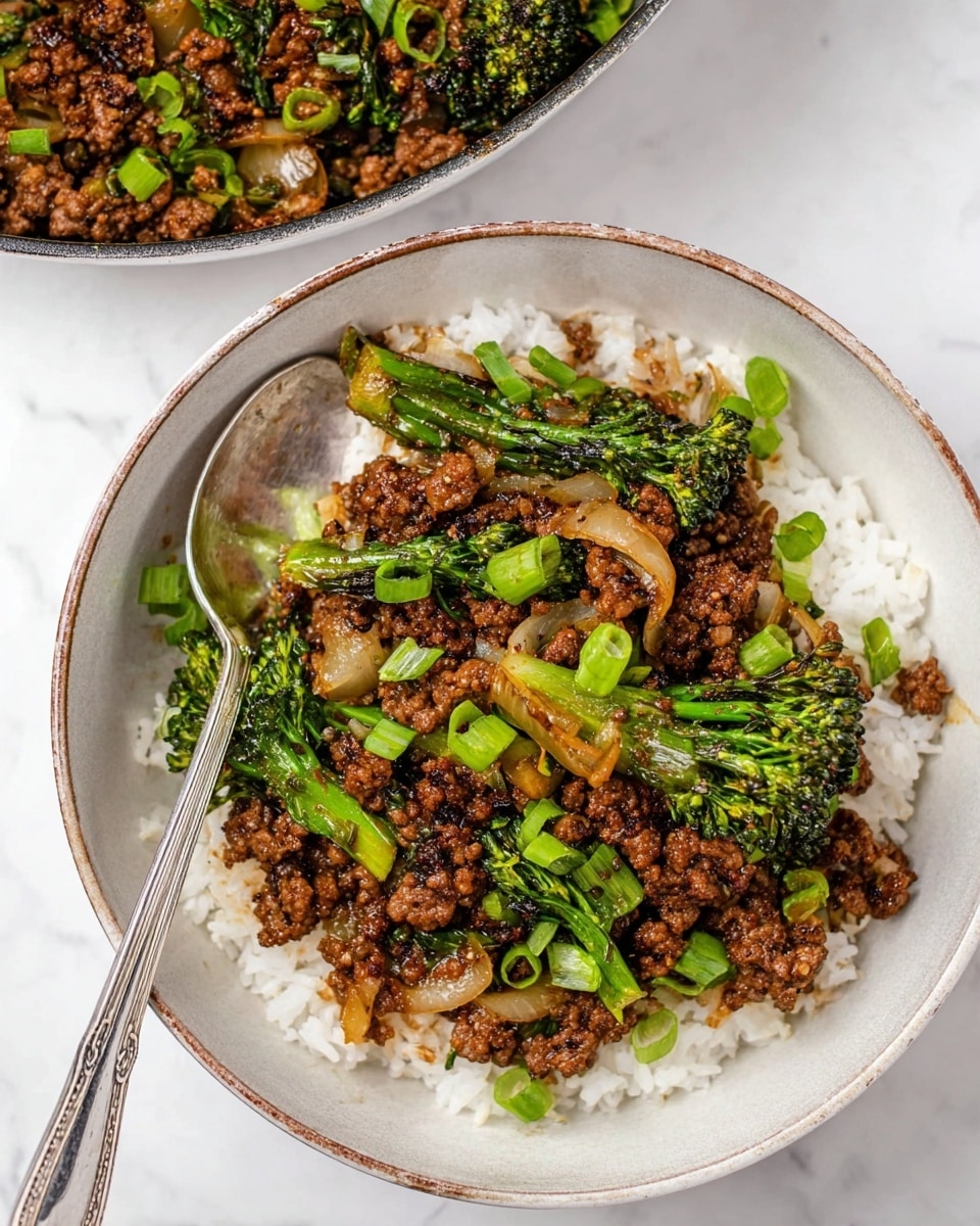 A top view of a white bowl filled with cooked white rice as the bottom layer, topped with a mix of dark brown cooked ground meat, green broccolini, sautéed onions in light brown and translucent colors, and sliced green onions scattered on top. A silver spoon rests inside the bowl on the left side. In the background, there is a white bowl containing more of the meat and vegetable mixture. Both bowls are placed on a white marbled surface. Photo taken with an iphone --ar 4:5 --v 7