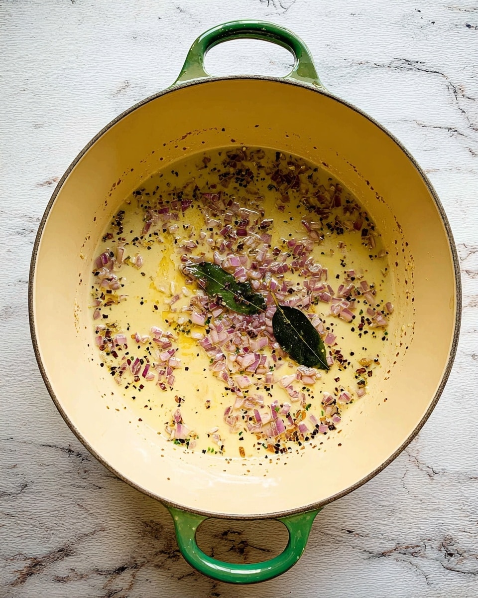 A large round light yellow pot with green handles sits on a white marbled wooden surface, containing a thin layer of light golden oil. Scattered over the oil are small pieces of finely chopped red onion and a single dark green bay leaf, creating a mix of light purple, green, and black dots across the bottom of the pot. The inside walls of the pot show slight browning from cooking. photo taken with an iphone --ar 4:5 --v 7