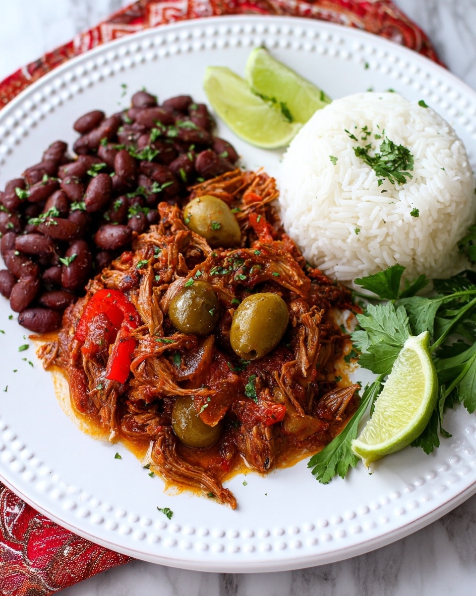 On a white plate with a dotted rim, there are three main parts visible. On the left side, there are dark red cooked beans scattered with small green parsley pieces on top. In the middle, a thick layer of shredded meat mixed with slices of red peppers, green olives, and some green capers is covered in a rich reddish-brown sauce, garnished with parsley leaves. On the right, a neat dome of white rice sits next to lime wedges and fresh green parsley leaves. The plate is placed on a white marbled surface, with part of a red and white cloth visible underneath. photo taken with an iphone --ar 4:5 --v 7