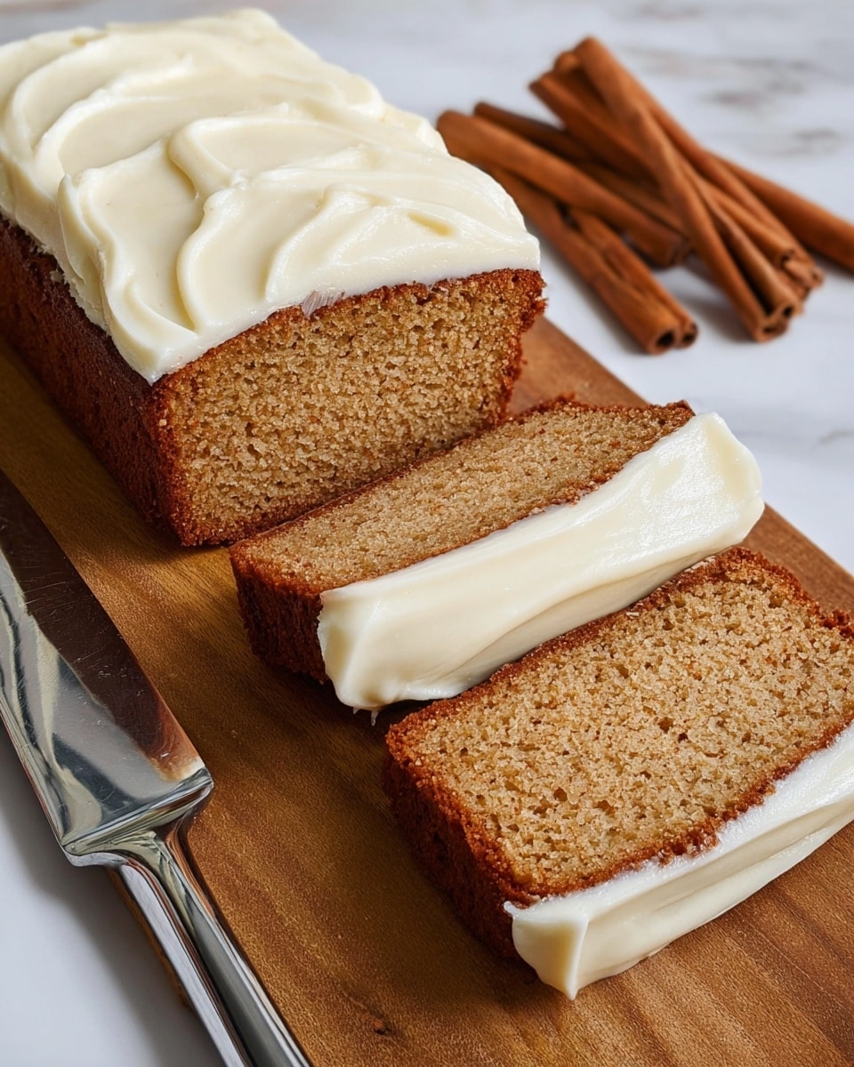 The image shows a loaf of light brown cake with a crumbly texture, topped with a thick layer of smooth white frosting spread in curves. Two slices are cut from the loaf, each with a thick white frosting layer on top and a rough brown edge from baking. The cake sits on a wooden board, with three sticks of cinnamon placed behind it on a white marbled surface. A shiny metal cake server lies next to the board, slightly reflecting the colors around it. The scene is cozy and warm, suggesting a fresh, homemade treat. Photo taken with an iphone --ar 4:5 --v 7