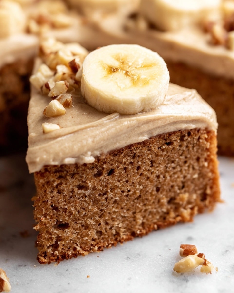 A square cake cut into nine pieces sits on white crinkled baking paper over a black wire rack, on a white marbled surface. The cake is topped with a thick layer of light tan frosting that looks creamy and smooth. Scattered on the frosting are small pieces of crushed nuts and a dusting of cinnamon powder. Three square pieces have thin banana slices on top. One piece is turned on its side showing a soft, light brown cake layer beneath the frosting. A silver fork is near the lower right corner, partly touching a cake slice. The lighting is soft and bright, giving the cake a fresh and inviting look. Photo taken with an iphone --ar 4:5 --v 7