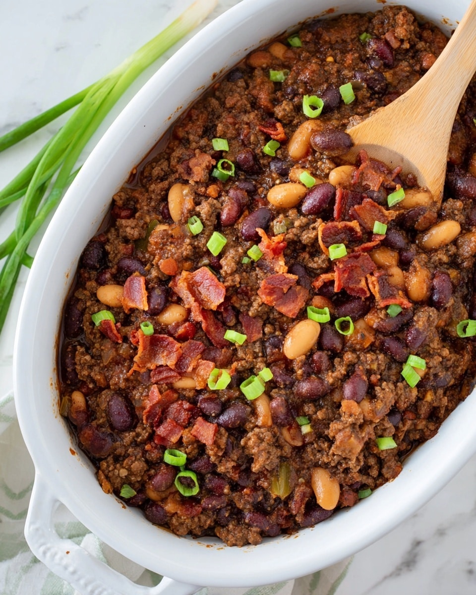 A white bowl filled with thick chili, showing layers of dark red kidney beans, light brown beans, chunks of browned meat, and flecks of onion, all covered in a rich brown sauce, topped with two green chive pieces crossed on top. The bowl is placed on a white plate, alongside two golden brown biscuits with a crisp texture. Under the plate, there is a green and blue plaid cloth. A blurred silver spoon is in the background resting on the white marbled surface, with a bottle of dark red sauce with a bright yellow label standing behind the bowl. Photo taken with an iphone --ar 4:5 --v 7